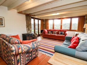 Un salon avec un canapé à motifs, un canapé rouge et un canapé bleu. On y trouve une table basse en bois, un tapis à rayures et un mur en pierre.
