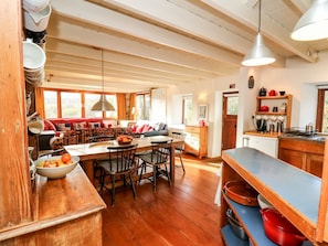 Une cuisine spacieuse avec un plancher en bois, un coin repas avec une grande table et des chaises, et une vue sur l’extérieur grâce à de grandes fenêtres.