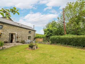 A stone house with a grassy yard, a patio with a table and chairs, and a wooden fence. - Buzzards Breg, Builth Wells (Builth Wells)