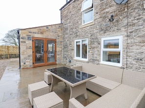 A stone building with a glass door, a patio with wicker furniture, and a stone wall. - Parkers House, Alston (Alston)