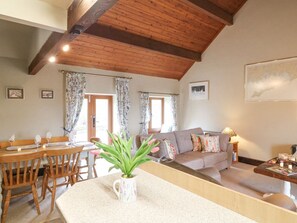 A dining area with a wooden table and chairs, a sofa, and a small table with a lamp. - Dove Cottage, near Waterhouses (Leek)