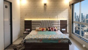 Un dormitorio con vista a la ciudad, ventilador de techo, cama con ropa de cama estampada y cabecera con iluminación integrada.