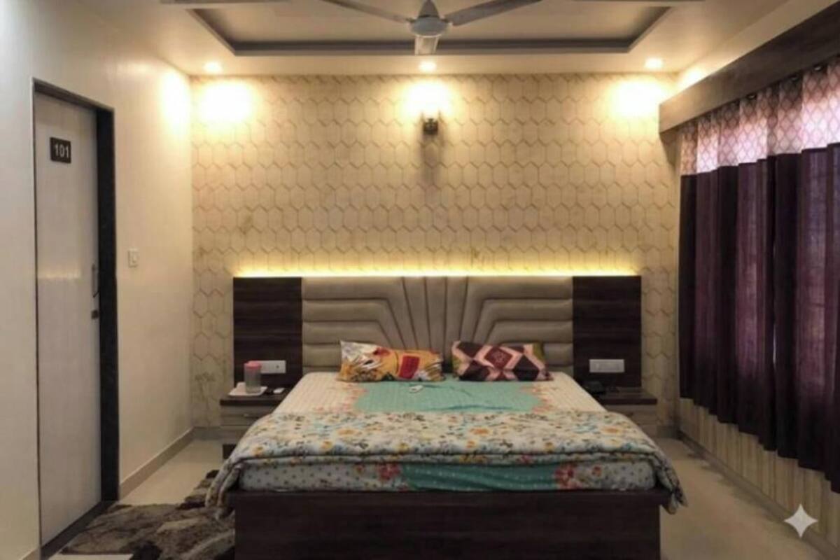 A bedroom with a bed, a ceiling fan, a headboard with built-in lighting, and a patterned wall.