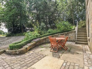 A patio with a table and chairs, surrounded by greenery and a stone wall.