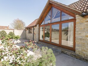 Un bâtiment en pierre avec un toit recouvert de tuiles, de grandes fenêtres en verre et un petit jardin agrémenté de plantes.