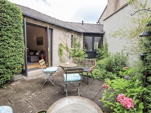 A cozy outdoor patio with a table and chairs, a garden with flowers, and a building entrance.