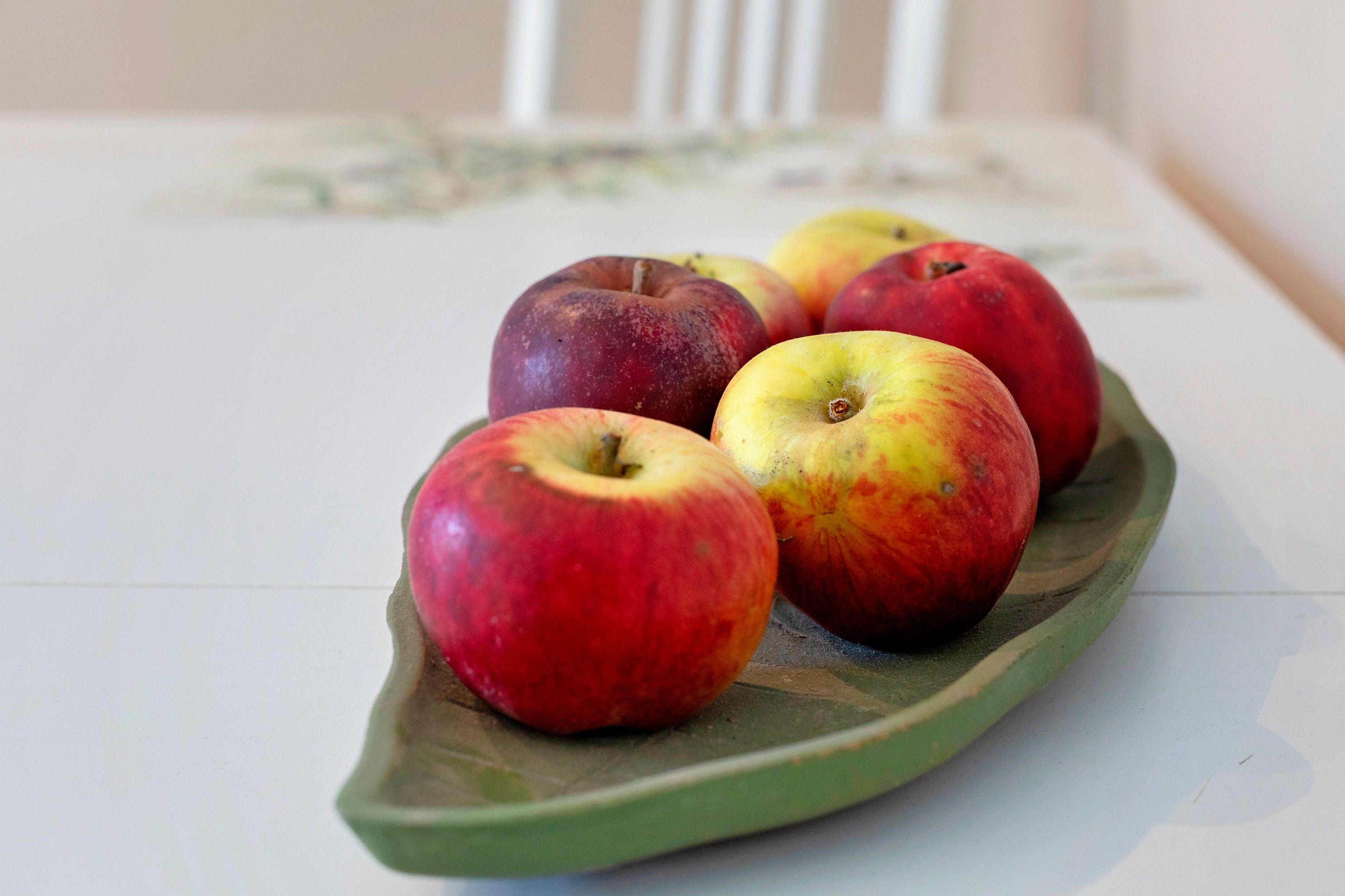 A green leaf-shaped plate with several apples on a white table.