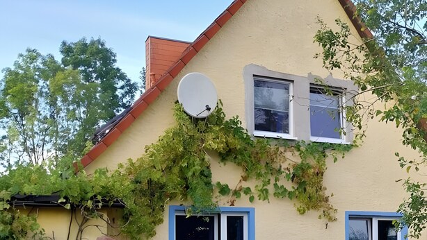 A house with a sloped roof, satellite dish, and a deck with chairs.