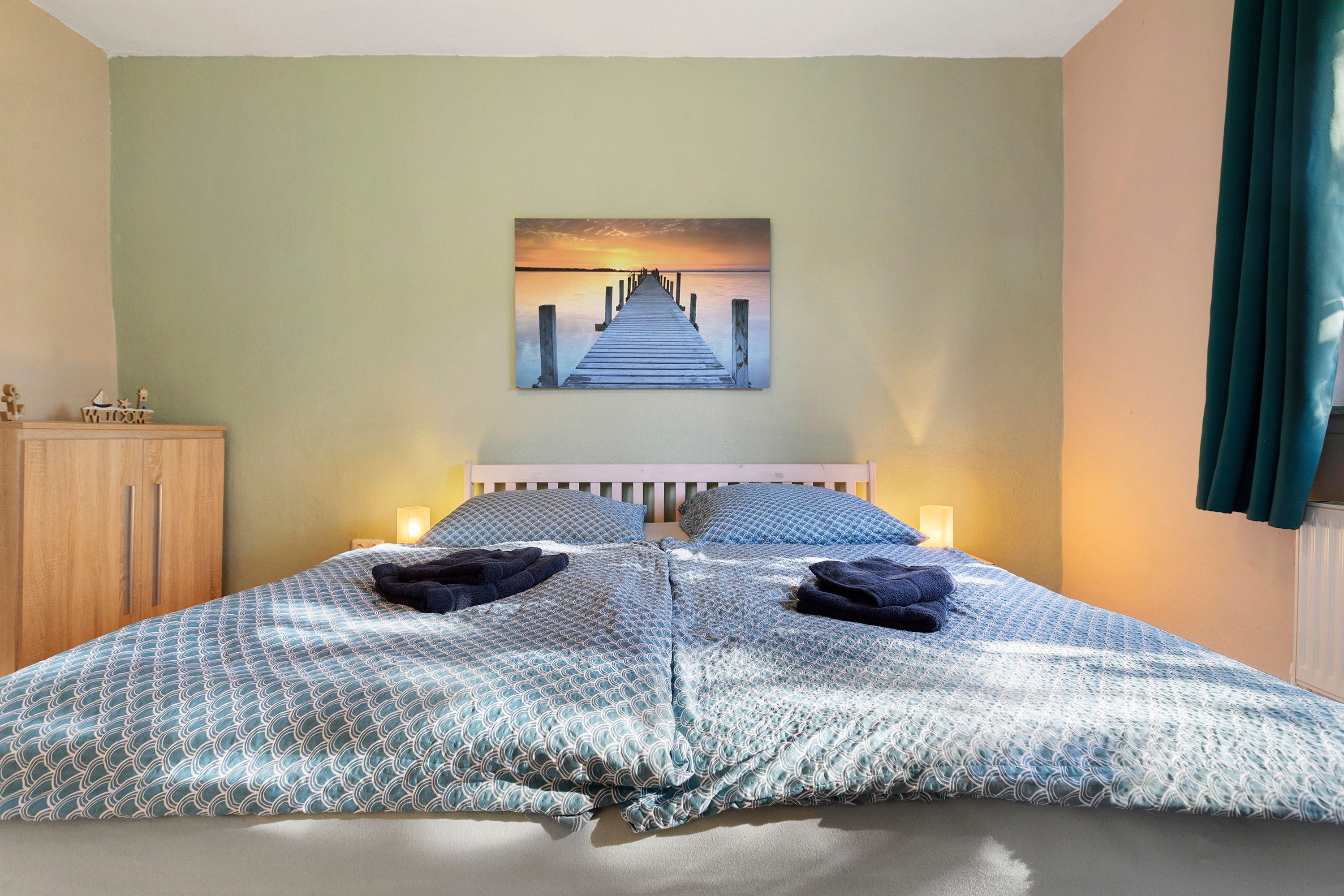 Ein Schlafzimmer mit einem Bett, Kissen, einem Nachttisch, einem Holzschrank, einem Gemälde und einem Vorhang.