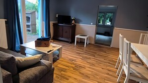 A living room with a sofa, a coffee table, a TV on a cabinet, a small table, and a window.
