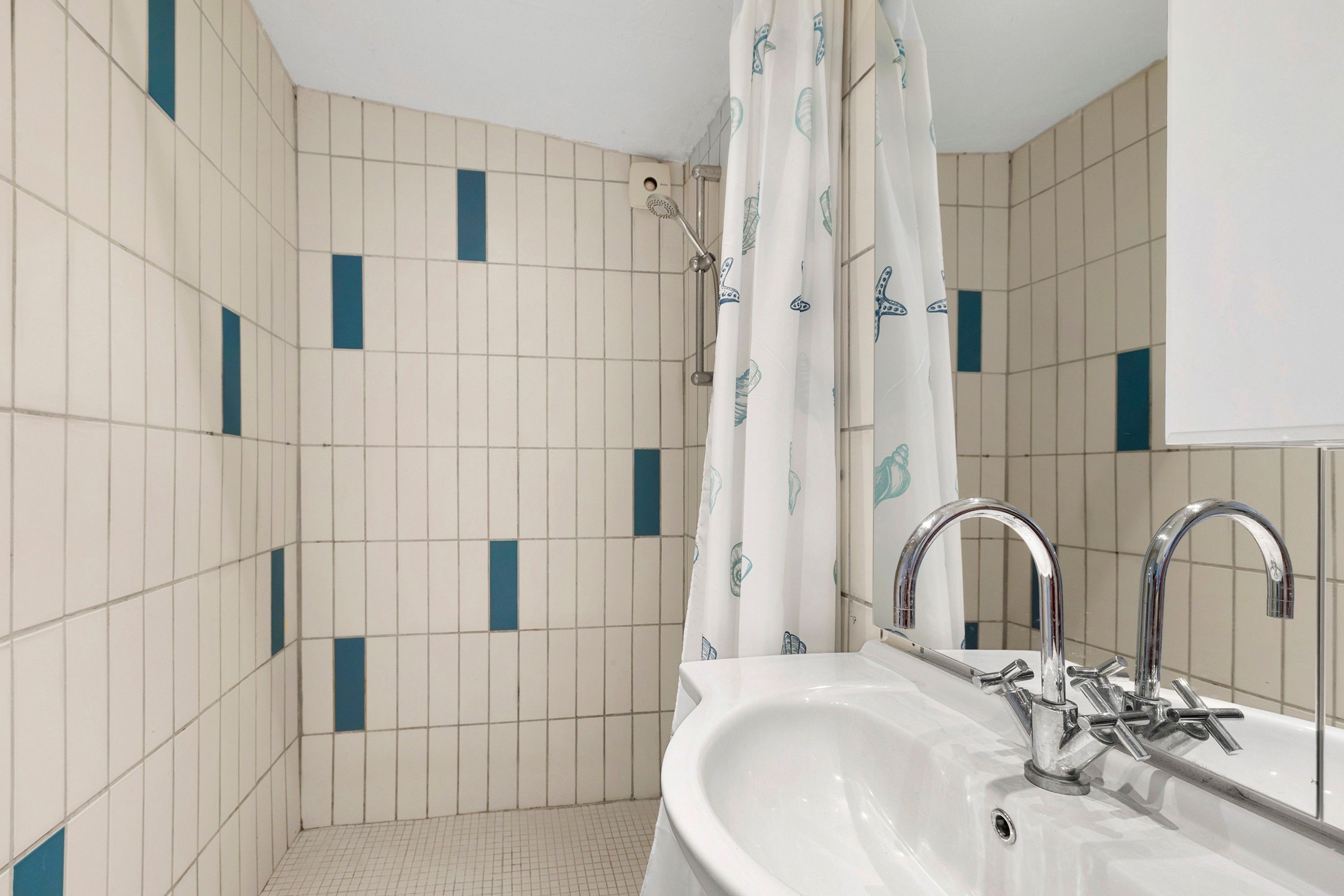 A bathroom with a white sink, chrome faucet, and a shower curtain with a pattern.