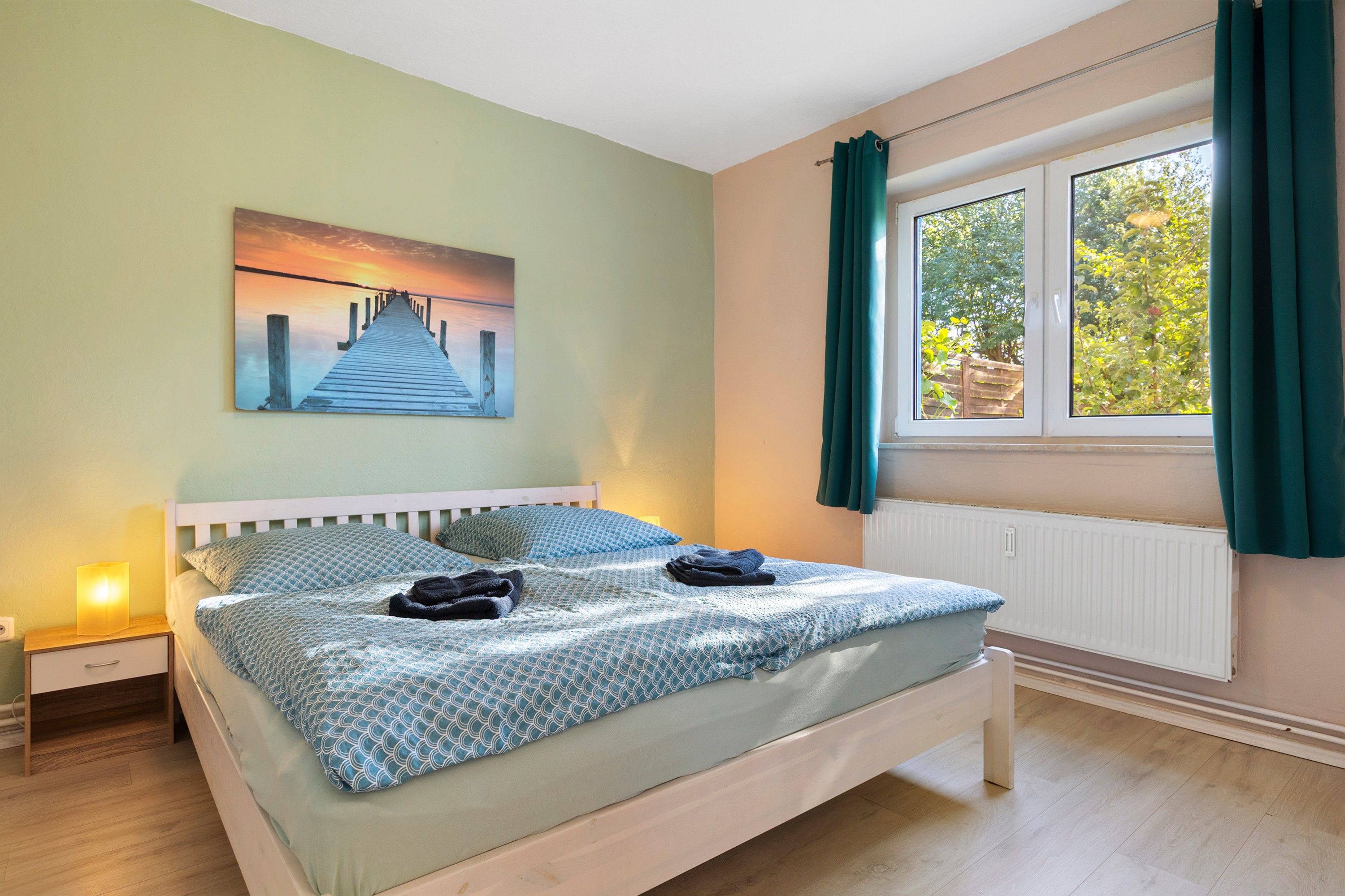 Una camera da letto con un letto, un comodino, una finestra con tende e un quadro appeso al muro.