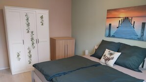 A bedroom with a bed, a wardrobe, a nightstand, and a painting of a sunset over a pier.