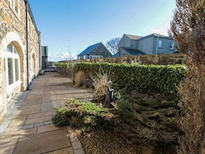 A stone pathway leading to a building with a stone wall and a hedge.