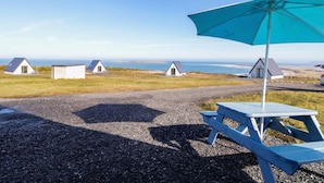 A gravel path leading to a row of small, white cottages with blue roofs, a picnic table, and a blue umbrella. - Cabin 4 Doire Chonair (Gortahork)