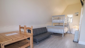 A room with a wooden table, a gray sofa, and a bunk bed. - Cabin 4 Doire Chonair (Gortahork)