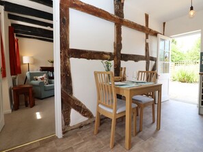A dining area with a wooden table and chairs, a lamp, a sofa, and a view of greenery outside. - Mortons Cottage, Castlemorton (Malvern)