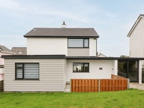 Una casa de dos pisos con techo plano, cerca de madera frontal y el número 17 visible en la pared.