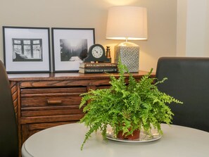 A dining table with a potted fern, a lamp, framed pictures, and books on a wooden sideboard. - Witts End, Marske-By-The-Sea (Redcar)