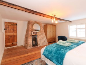 Ein Schlafzimmer mit Kamin aus Backsteinen, einem Holzschrank und einem Bett mit blauer Bettwäsche.
