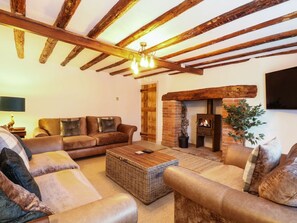 Ein gemütliches Wohnzimmer mit Kamin, Ledersofas, einem Holztisch und freiliegenden Holzbalken.
