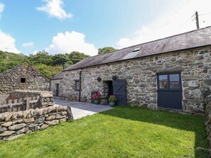 A stone building with a sloped roof, a wooden fence, and a paved pathway leading to the entrance. - Beudy Bach, Llanfair (Llanbedr)