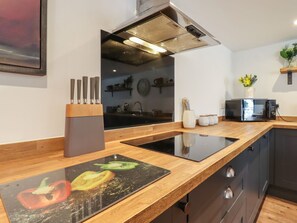 A modern kitchen with a wooden countertop, a black induction cooktop, a stainless steel range hood, and a microwave. - The Old Dairy, Adiham, near Wingham, Kent. (Canterbury)