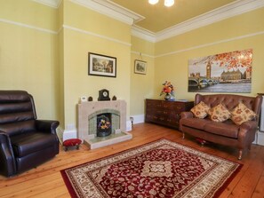 A living room with a fireplace, a brown leather sofa, a red and beige rug, and a painting of a cityscape. - Mullans, Southport, Merseyside (Southport)