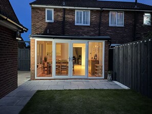 A house with a glass-enclosed patio area, a brick exterior, and a visible kitchen.
