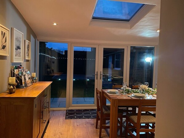 A dining area with a table set for two, a wooden cabinet with items on top, and a skylight above.