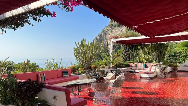 An outdoor patio with red flooring, seating areas, and a view of the ocean. - Villa Luna Rossa, Capri (Capri)