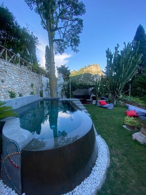 A swimming pool with a stone wall, a tree, and a mountain in the background. - Villa Luna Rossa, Capri (Capri)