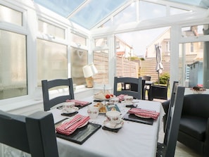 A conservatory with a table set for tea, chairs, and a view of the outside. - Pier View: Cozy Retreat in Paignton (Paignton)