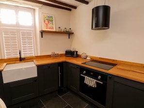 Une cuisine avec un plan de travail en bois, une cuisinière noire, un évier blanc et une fenêtre avec des stores.