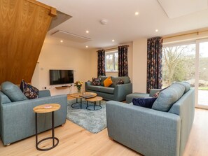Ein modernes Wohnzimmer mit einer Sofagarnitur, einem Fernseher und einem großen Fenster mit Vorhängen.