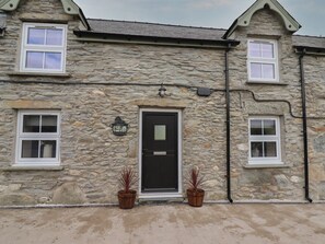 A stone building with a black door, white windows, and potted plants. - Rhos Las, Cerrigydrudion. 4bed (Corwen)