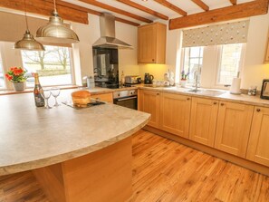 A kitchen with wooden cabinets, a curved island, pendant lighting, and a view of the outdoors. - COTTAGE, WiFi, enclosed patio, near Cowling (Keighley)