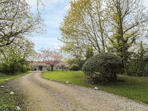A gravel driveway leading to a house with a red roof, surrounded by trees and a well-maintained lawn. - Robin Cottage, Morpeth (Morpeth)