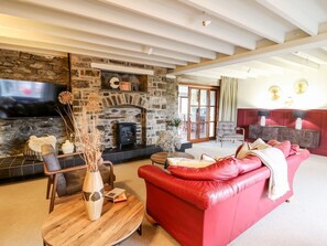 A living room with a stone fireplace, a red leather sofa, a wooden coffee table, and a flat-screen TV mounted on the wall. - Dant Y Llew, Bow Street, Wales (Bow Street)