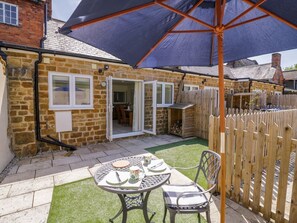 A stone house with a patio, a table with chairs, and a wooden fence. - Charming Treacle Cottage Retreat (Warwick)