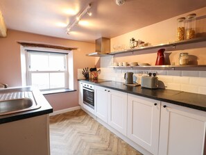 A kitchen with white cabinets, a black countertop, a window, and a built-in oven. - The Loft at The Old Dog Thorpe (Ashbourne)