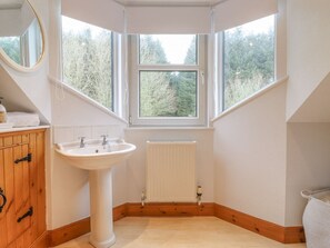 Ein Badezimmer im Eckbereich mit einem weißen Waschbecken, einem Holzkabinent und einem Fenster mit Blick auf Bäume.
