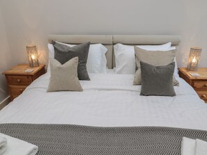 A neatly made bed with a patterned bedspread, two bedside tables with lamps, and a headboard. - The Coach House, Bamburgh (Bamburgh)