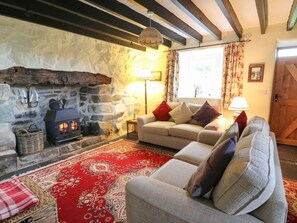 A cozy living room with a stone fireplace, a sofa, a red patterned rug, and a wooden ceiling. - Tyn Y Graig, Fairbourne (Arthog)