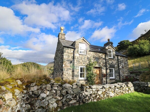 A stone house with a stone wall in front, a wooden door, and a window. - Tyn Y Graig, Fairbourne (Arthog)