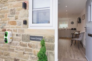 Eine Steinmauer mit einem Fenster, einer Tür, einer kleinen Zimmerpflanze und einem Schild mit der Aufschrift 'Eames Cottage'.