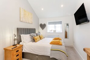 Ein Schlafzimmer mit Bett, Nachttisch, Lampe, Kunstwerk, Herz-Dekoration, Fenster und Fernseher.