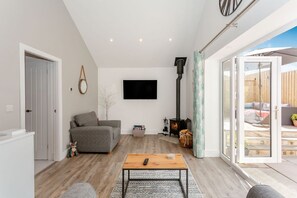 Ein modernes Wohnzimmer mit einer Couch, einem Kamin, einem Fernseher und einer Schiebetür zu einem Außenbereich.