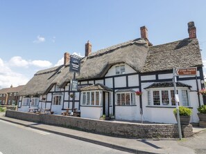 Eine traditionelle Tavern mit Strohdach und mehreren Sitzbereichen, mit einem Schild, das den Weg zur Thatch Tavern aus dem 13. Jahrhundert weist.