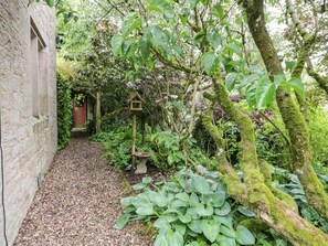 A garden path with a stone wall, a wooden door, and lush greenery. - The Lodge, Greystoke (Penrith)